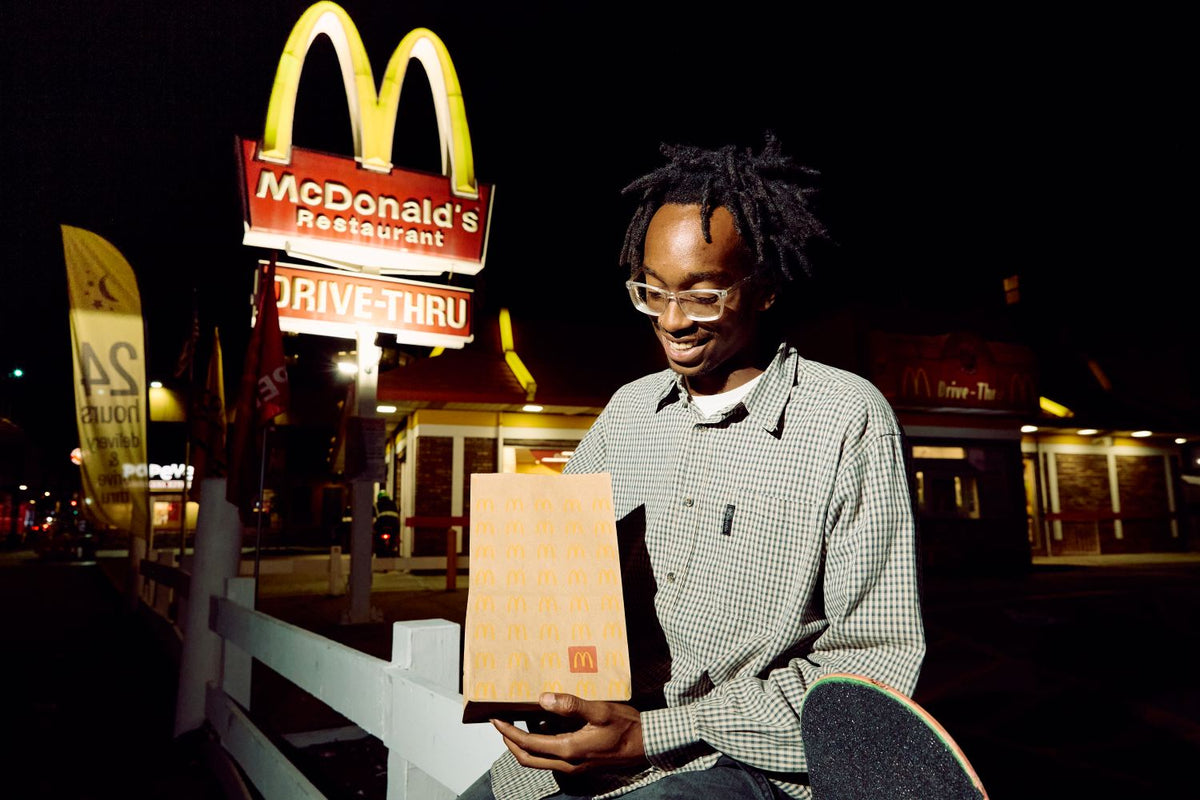 Still from the campaign film: a man carrying a red McDonald's skateboard past Fries, Golden Arch and McFlurry neons