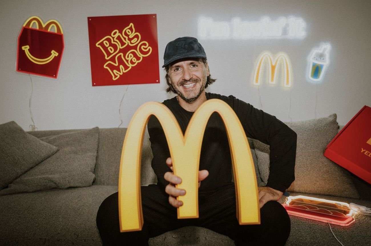Jeremy, founder of Yellowpop, on a sofa holding the Golden Arches sign, with the Happy Meal, Big Mac, I'm Lovin' It and McFlurry neons on the wall behind him